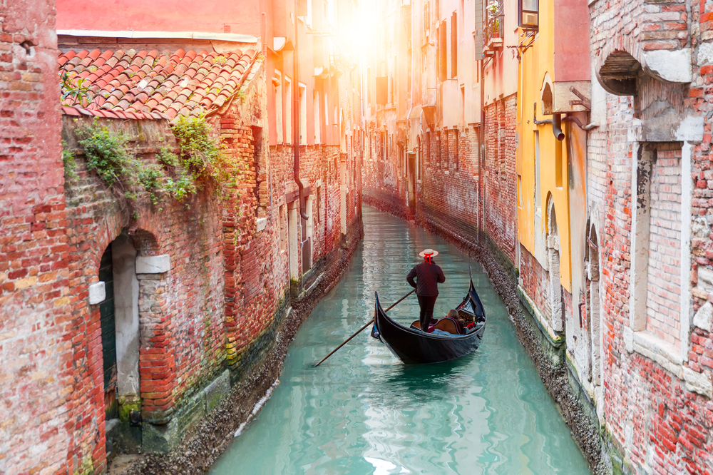 Venetian gondolier punting gondola through green canal waters of Venice Italy