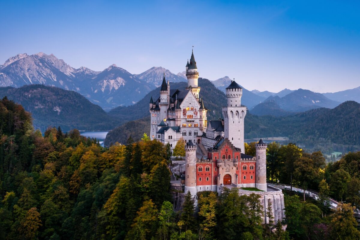 Neuschwanstein Castle with its white brick facades and black spires with the alpine mountains in the background.